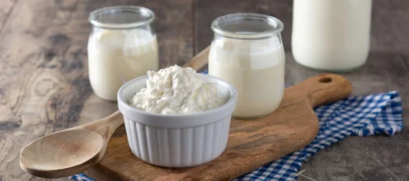 Nódulos de kéfir de leche en recipiente blanco sobre tabla de madera junto a frascos de vidrio